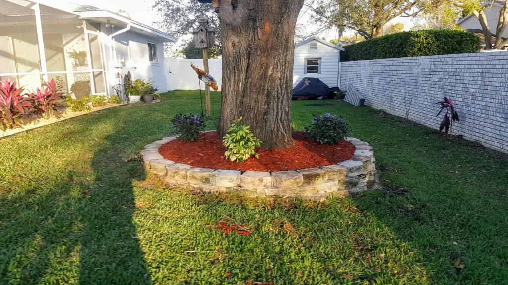 Circular landscape curbing around a large tree with red mulch and flowers