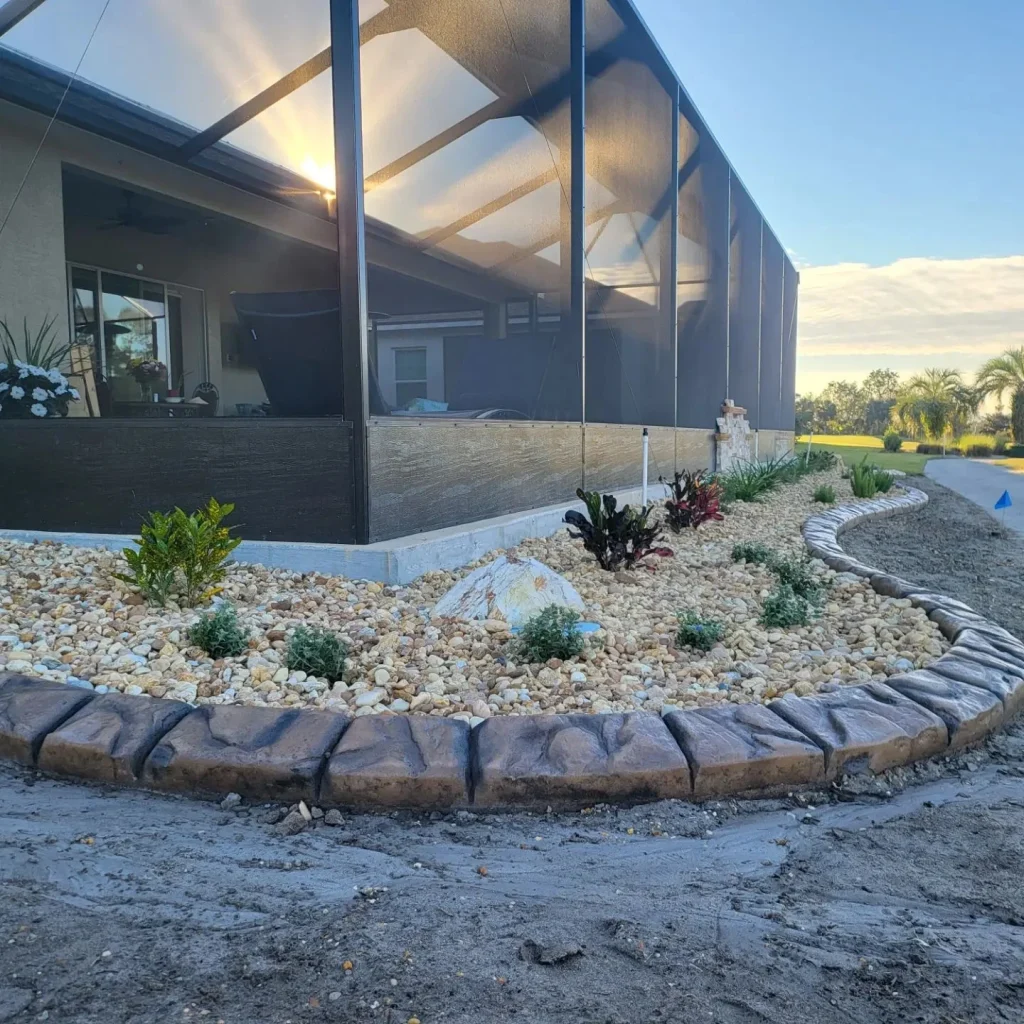 Screened patio landscape bed with concrete curbing, rock, and new plants